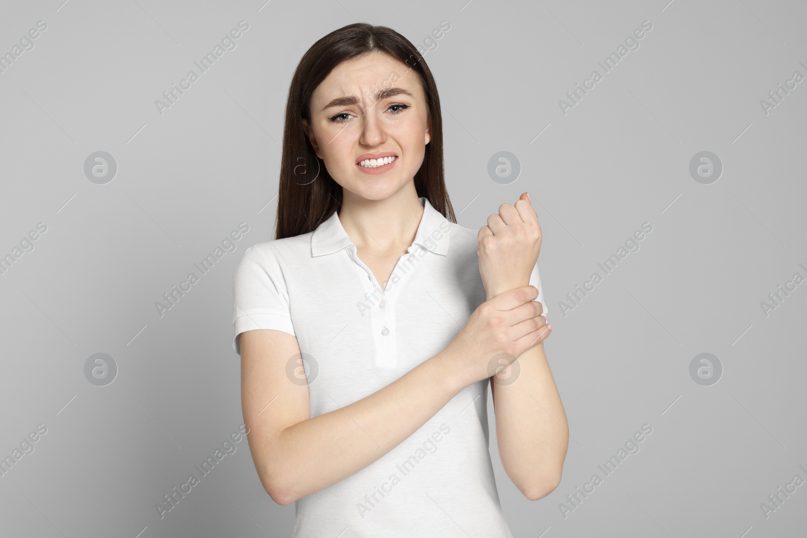 Photo of Young woman suffering from pain in her hand on light grey background. Arthritis symptoms