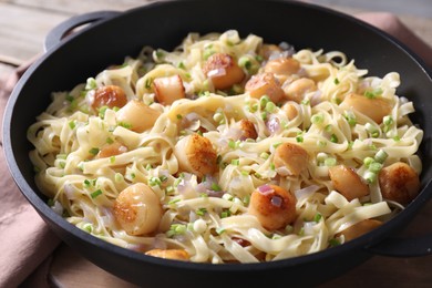 Delicious scallop pasta with onion in pan on table, closeup