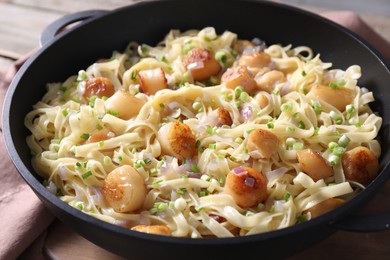 Photo of Delicious scallop pasta with onion in pan on table, closeup