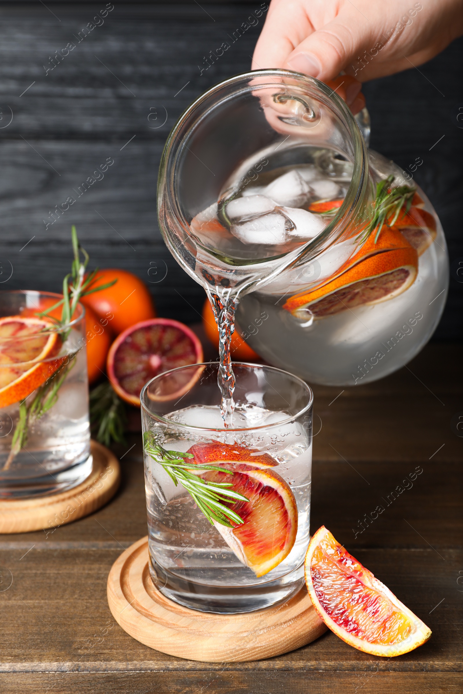 Photo of Woman pouring refreshing drink with sicilian orange from jug into glass at wooden table, closeup