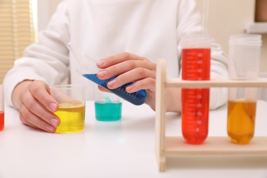 Photo of Girl mixing colorful liquids at white table indoors, closeup. Chemical experiment set for kids