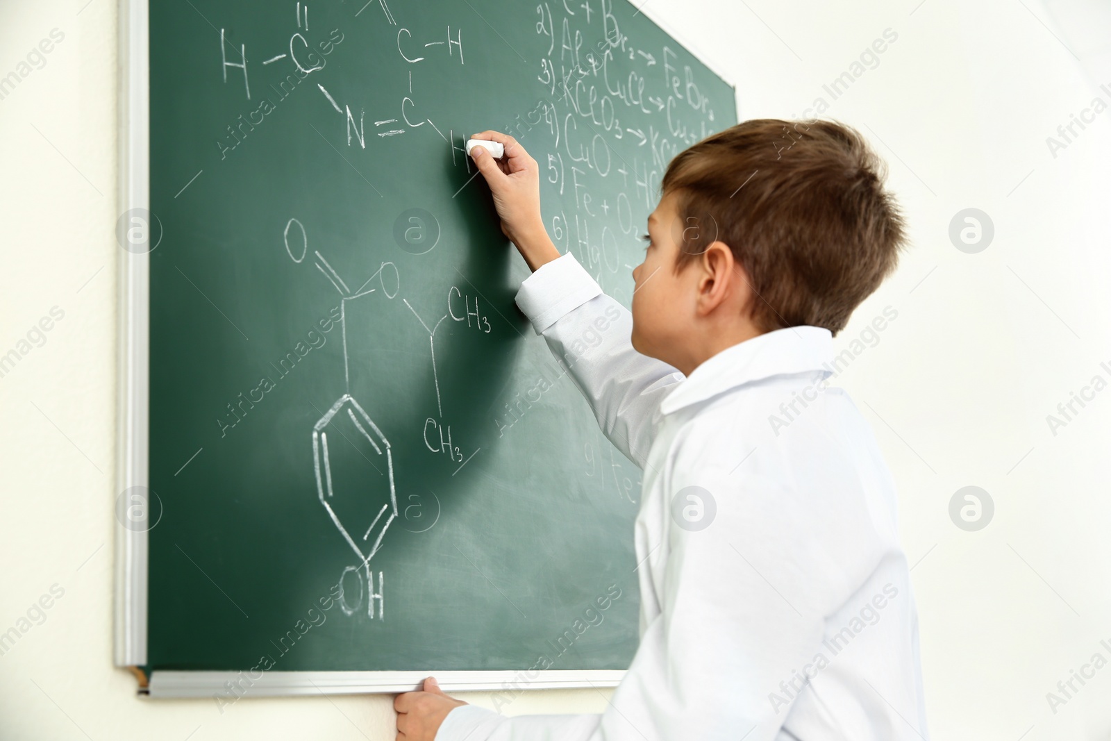 Photo of Schoolboy writing formula on blackboard in chemistry class