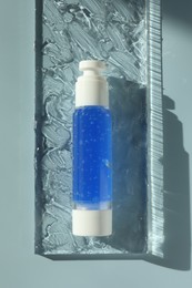 Bottle of cosmetic product on light blue background, top view