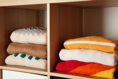 Photo of Stacks of folded winter clothes on shelves in wardrobe