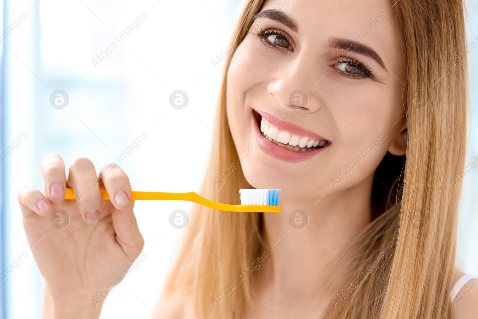 Photo of Young woman brushing her teeth indoors