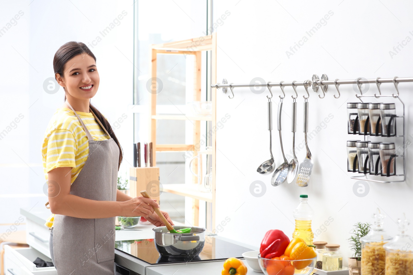 Photo of Young woman cooking tasty soup in kitchen