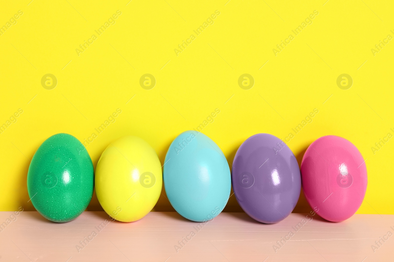 Photo of Easter eggs on pink wooden table against yellow background, space for text