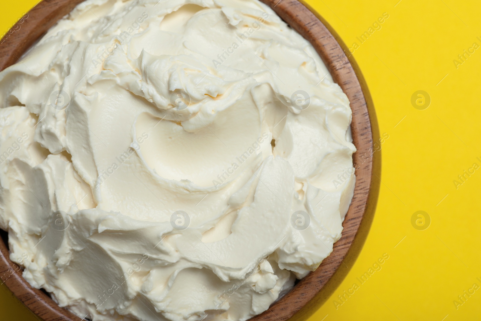 Photo of Bowl of tasty cream cheese on yellow background, top view