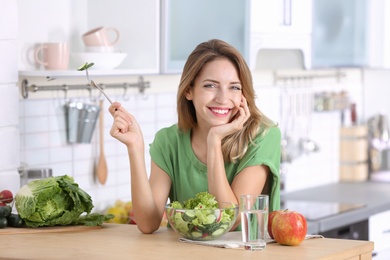 Woman eating vegetable salad at table in kitchen. Healthy diet