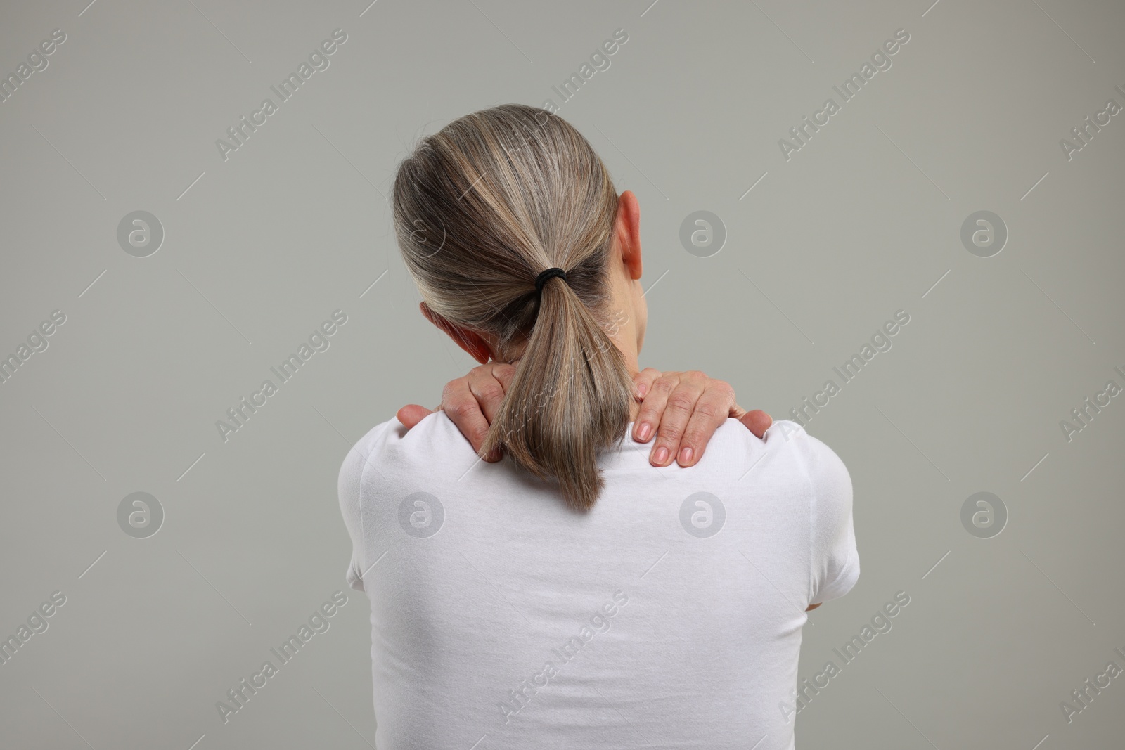 Photo of Mature woman suffering from pain in her neck on grey background, back view