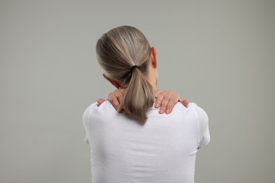 Mature woman suffering from pain in her neck on grey background, back view