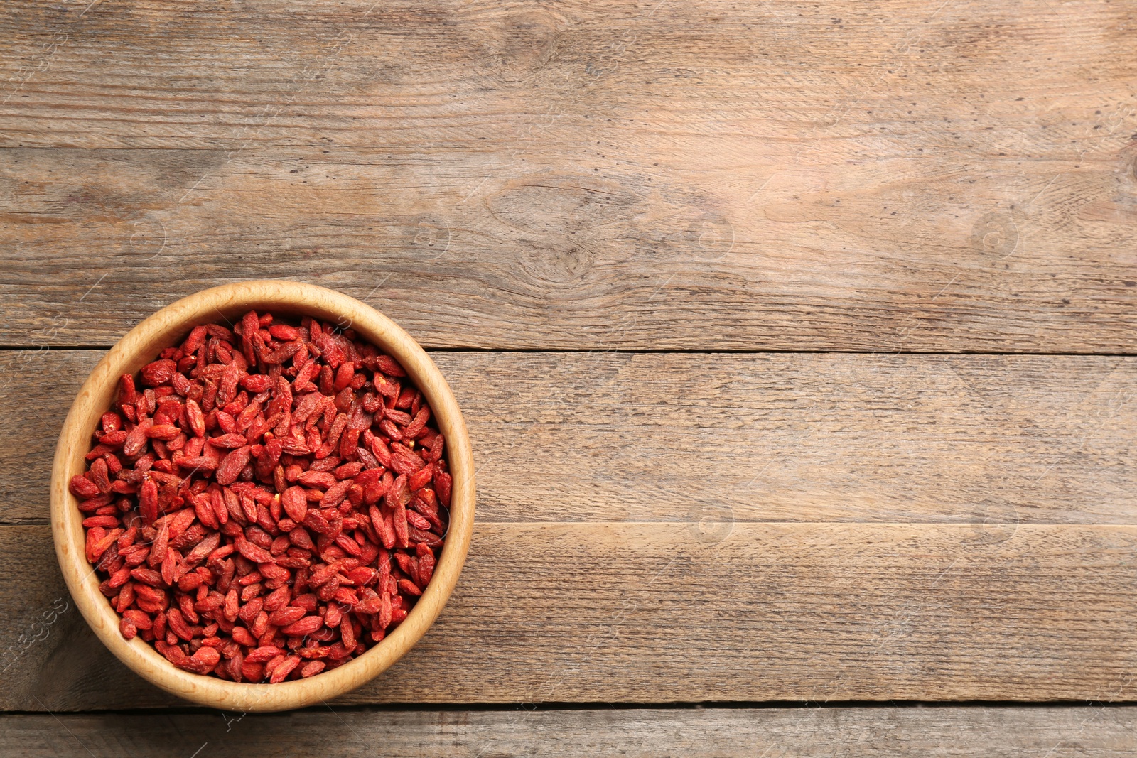 Photo of Bowl of dried goji berries on wooden table, top view with space for text. Healthy superfood