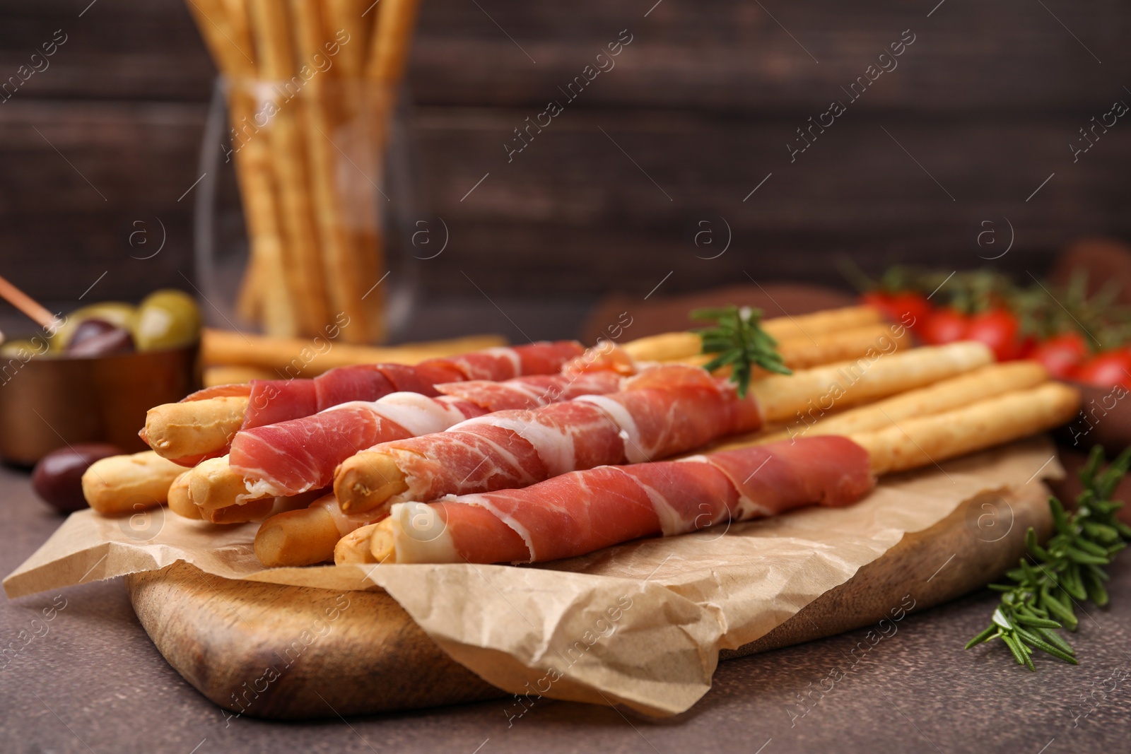 Photo of Delicious grissini sticks with prosciutto and ingredients on brown textured table