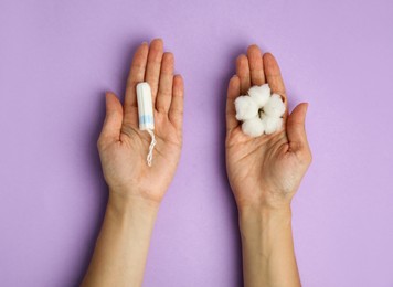 Top view of woman holding tampon and cotton flower on lilac background, closeup