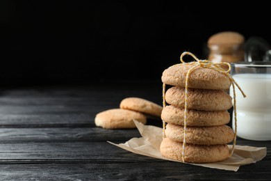 Delicious sugar cookies and glass of milk on black wooden table, space for text