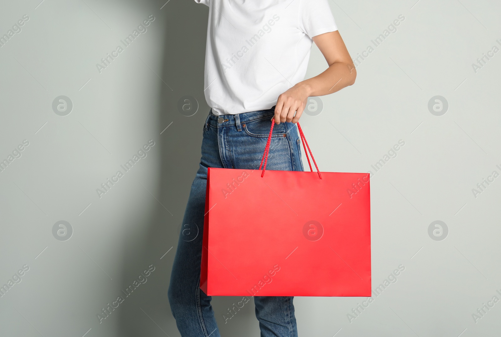 Photo of Woman with paper shopping bag on light grey background, closeup