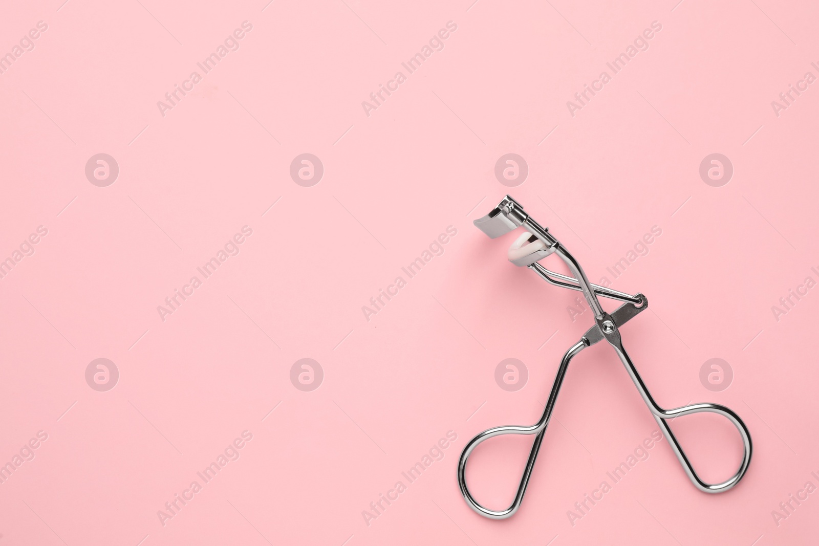 Photo of Eyelash curler on pink background, top view. Space for text