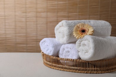 Photo of Rolled terry towels and flower on white table indoors, space for text