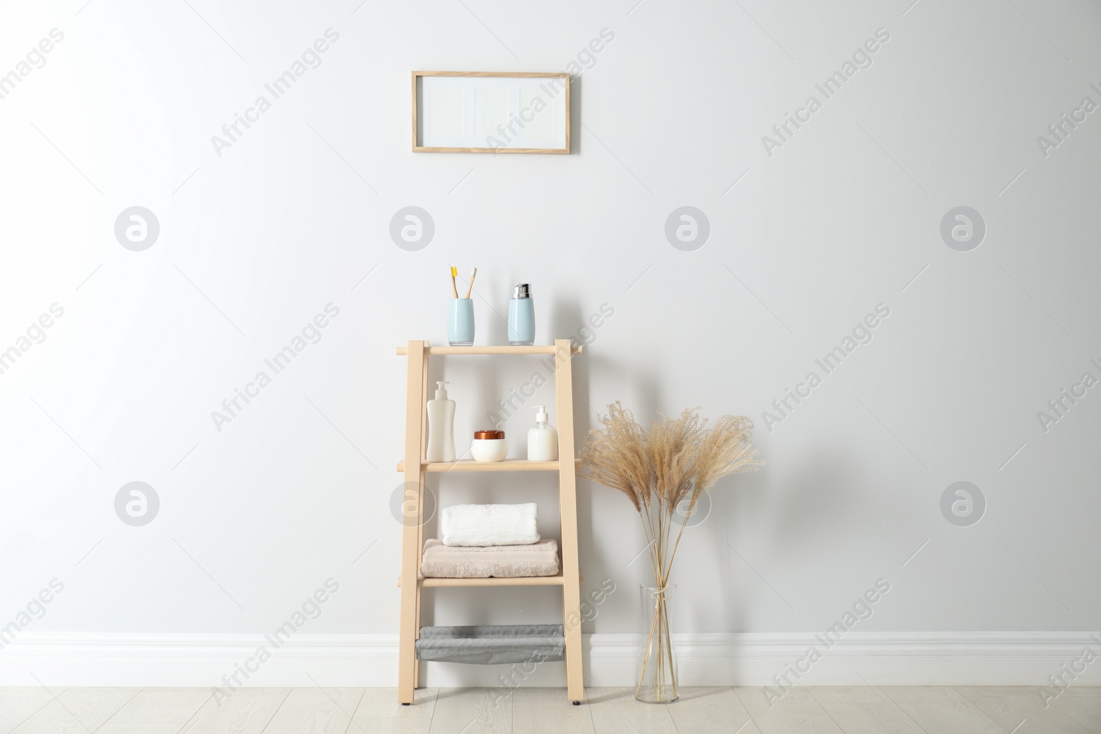 Photo of Wooden shelving unit with toiletries near white wall indoors. Bathroom interior element