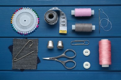 Flat lay composition with thimbles and different sewing tools on blue wooden table