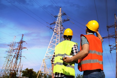 Professional electricians in uniforms near high voltage towers