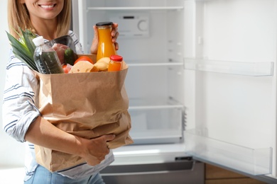 Woman with paper bag full of products near refrigerator in kitchen, closeup