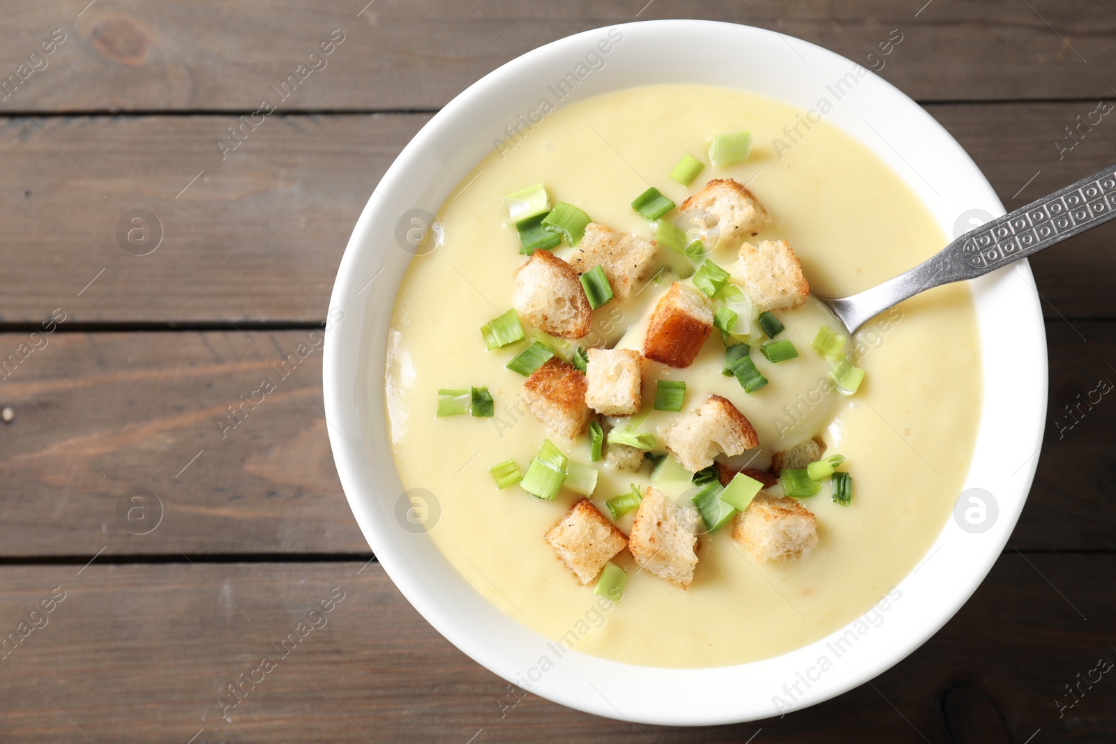 Photo of Tasty potato soup with croutons and spoon in bowl on wooden table, top view