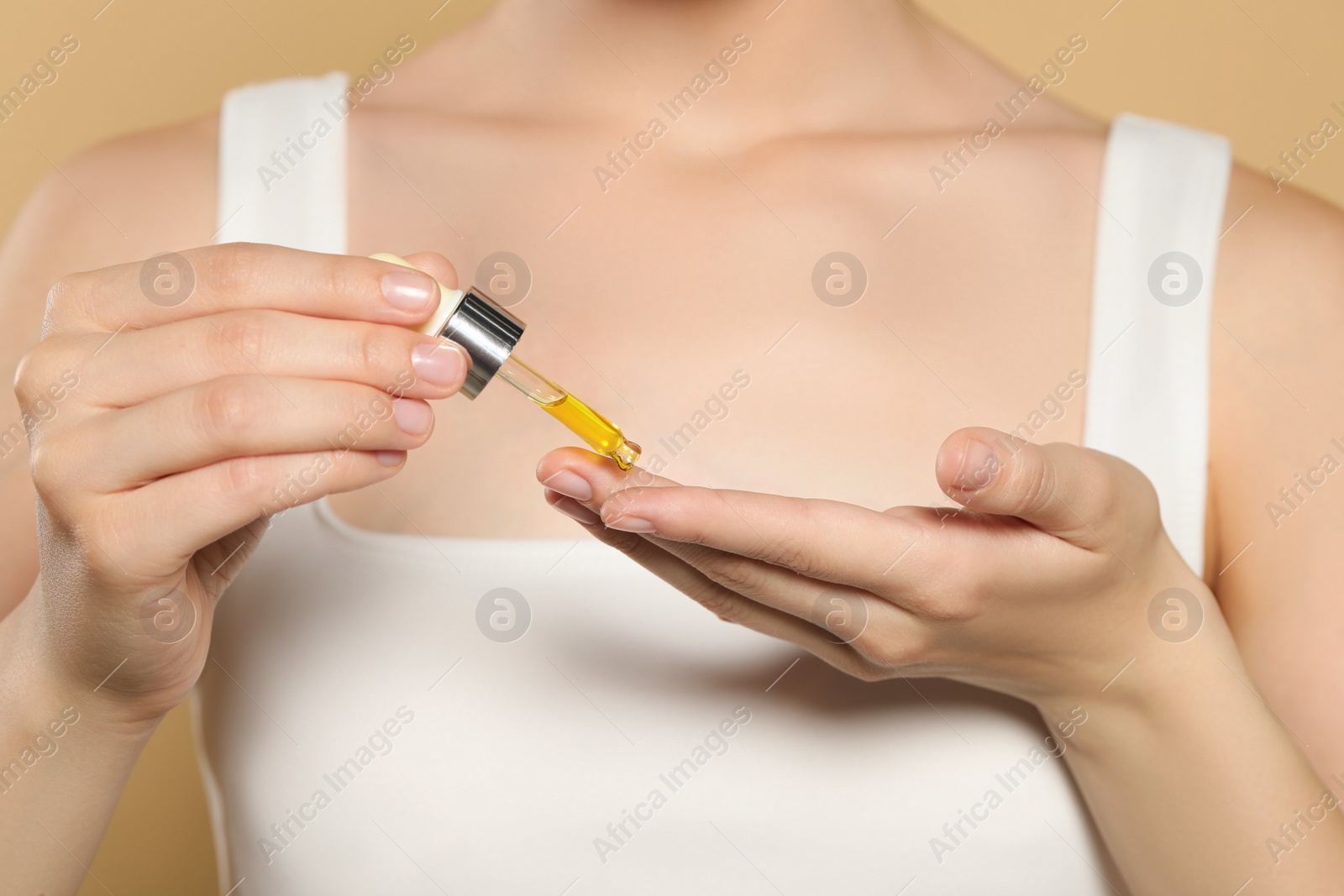 Photo of Young woman applying essential oil onto hand on beige background, closeup