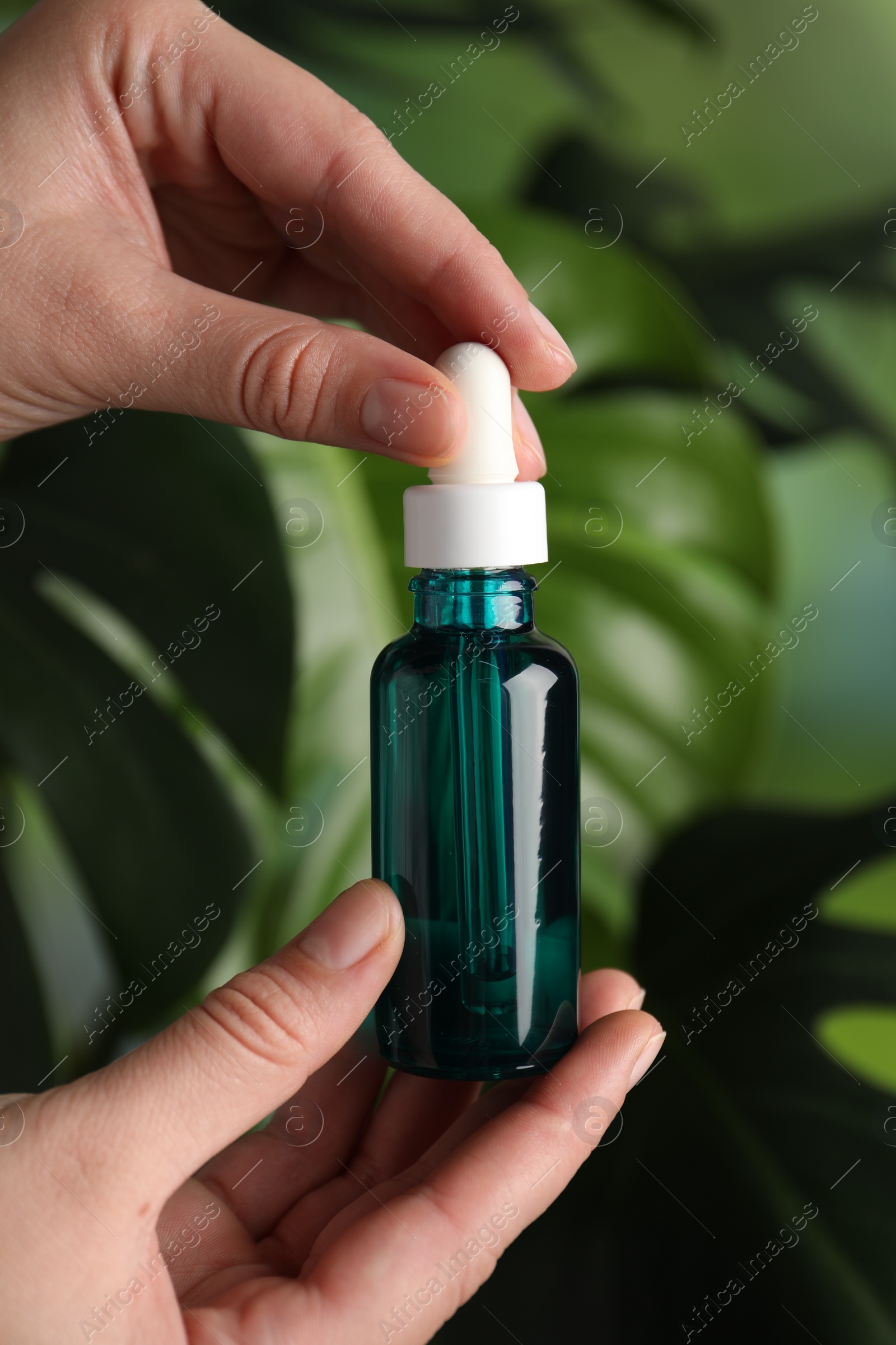 Photo of Woman with bottle of cosmetic serum on green background, closeup