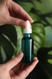 Photo of Woman with bottle of cosmetic serum on green background, closeup