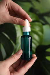 Woman with bottle of cosmetic serum on green background, closeup