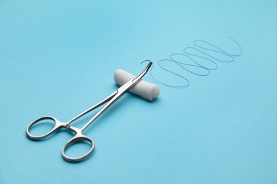 Photo of Forceps with suture thread and bandage roll on light blue background. Medical equipment