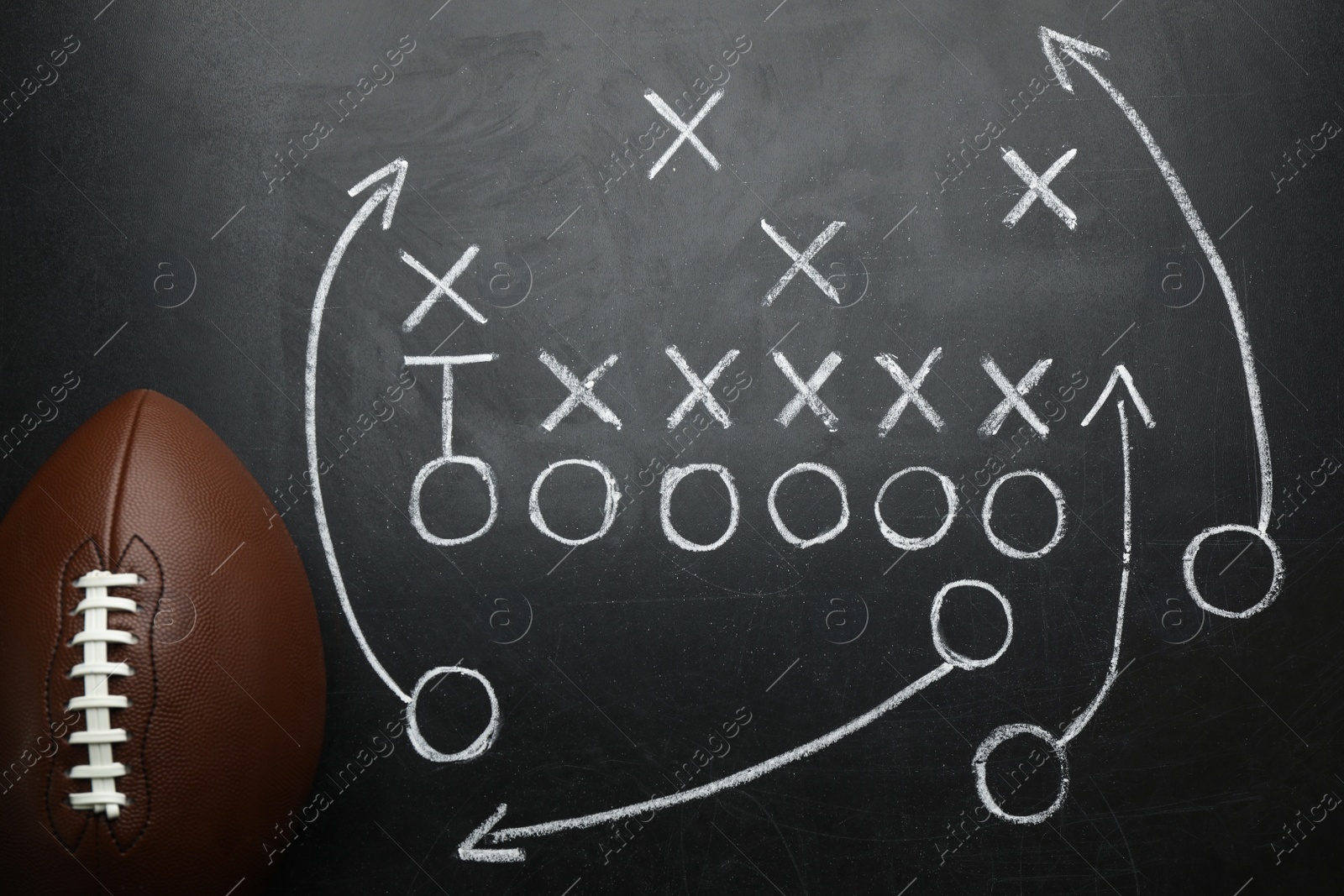 Photo of Rugby ball and drawn American football strategy game on black chalkboard, top view