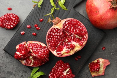 Photo of Fresh pomegranates and green leaves on grey table, top view
