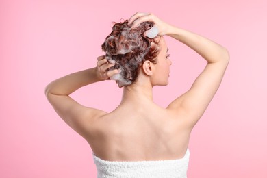 Young woman washing her hair with shampoo on pink background, back view