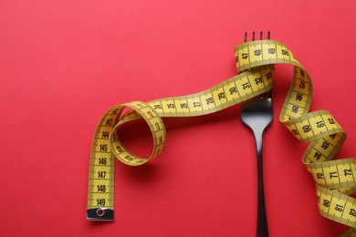 Photo of Fork with measuring tape on red background, top view. Diet concept