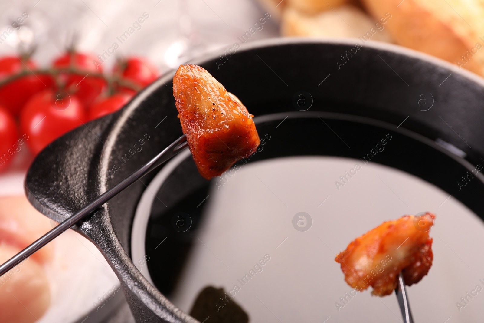 Photo of Fondue pot, forks with fried meat pieces and other products on table, closeup