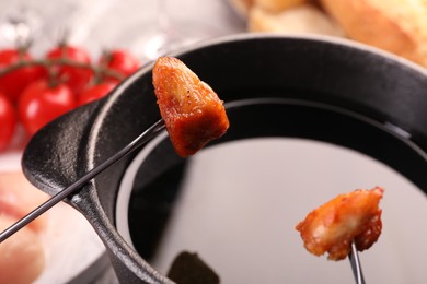 Fondue pot, forks with fried meat pieces and other products on table, closeup