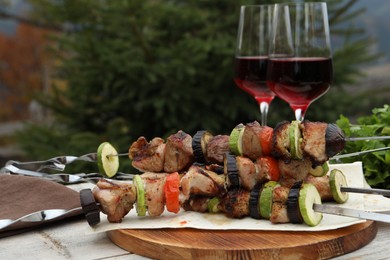 Photo of Metal skewers with delicious meat, vegetables and wine served on wooden table outdoors