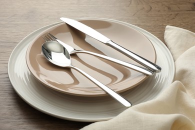 Clean plates and cutlery on wooden table, closeup