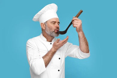 Photo of Chef in uniform tasting something on light blue background