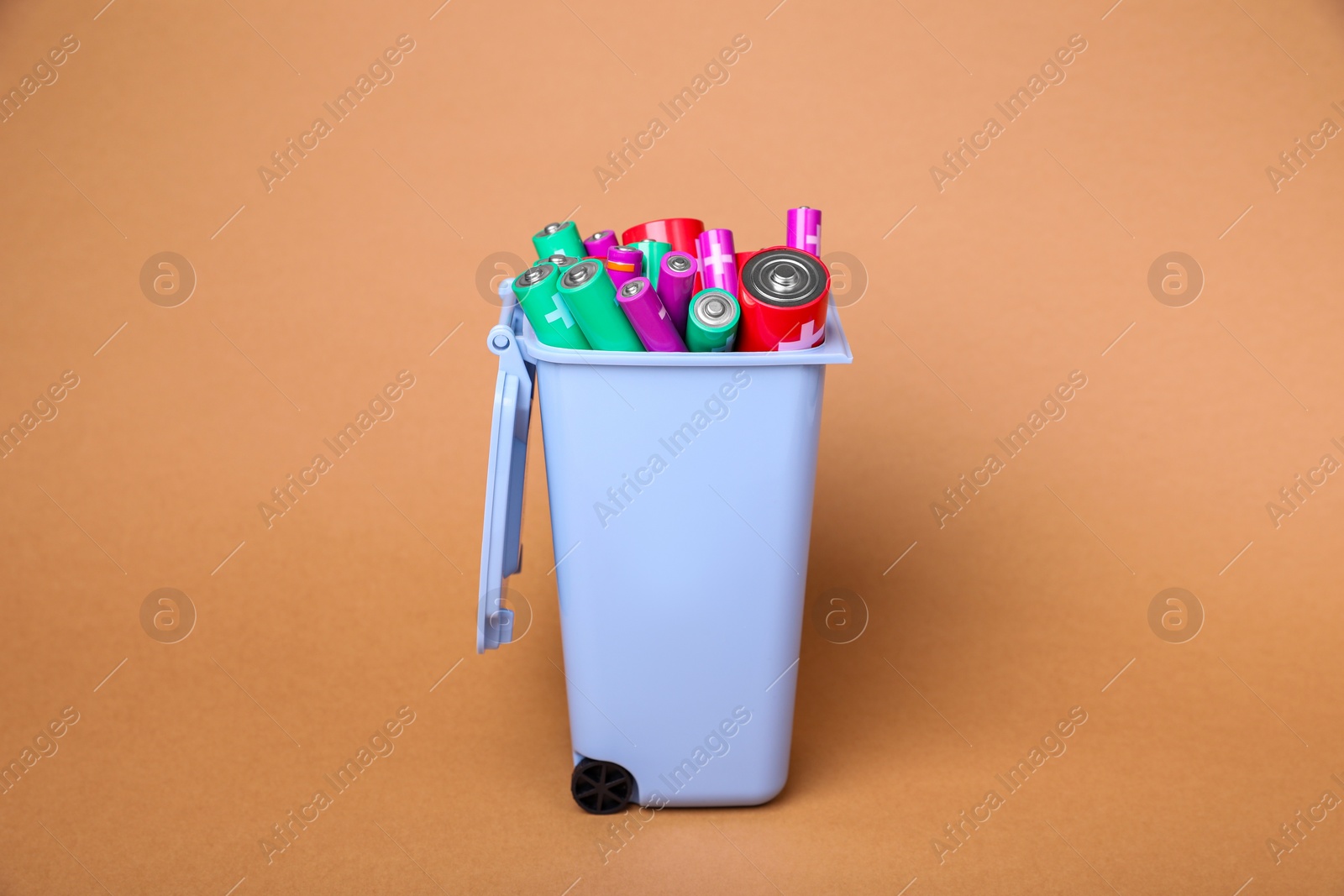 Photo of Many used batteries in recycling bin on coral background