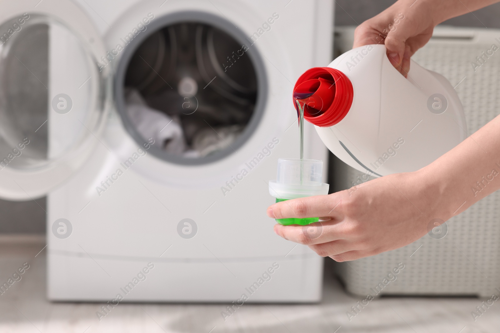 Photo of Woman pouring fabric softener from bottle into cap for washing clothes indoors, closeup. Space for text