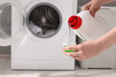 Photo of Woman pouring fabric softener from bottle into cap for washing clothes indoors, closeup. Space for text