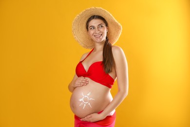 Photo of Young pregnant woman with sun protection cream on belly against yellow background