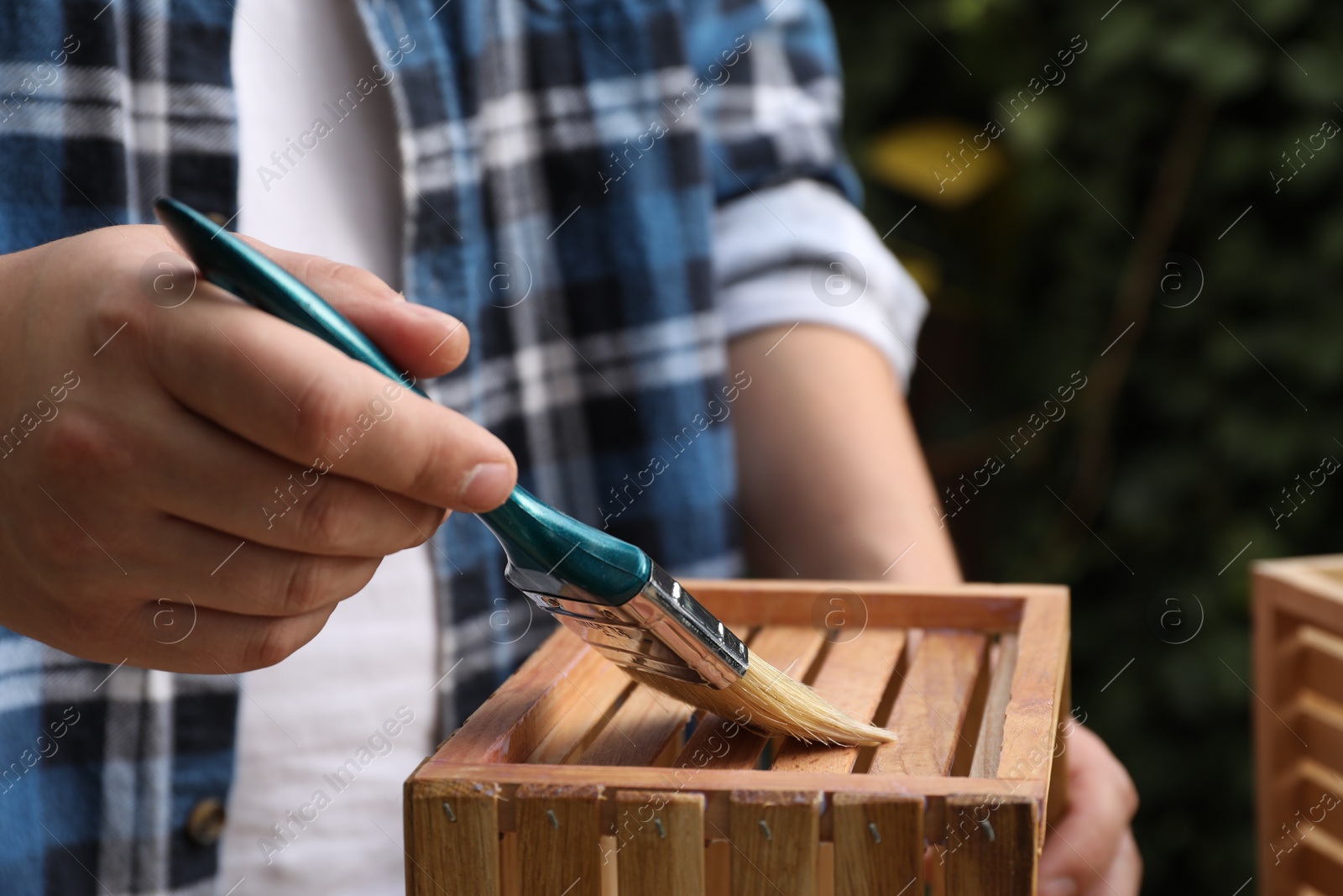 Photo of Man applying varnish onto wooden crate against blurred background, closeup