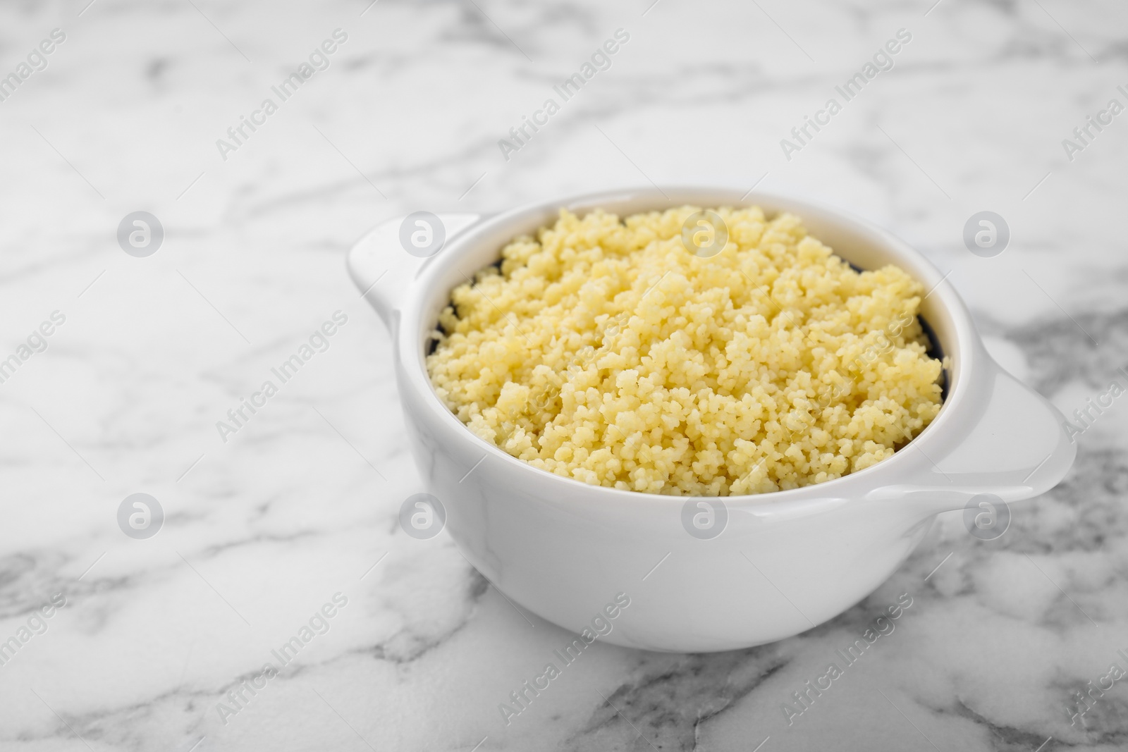 Photo of Bowl of tasty couscous on white marble table, closeup. Space for text