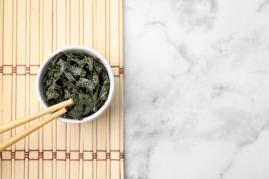 Chopped nori sheets with chopsticks on white marble table, top view. Space for text