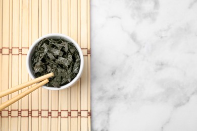 Photo of Chopped nori sheets with chopsticks on white marble table, top view. Space for text