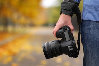 Photo of Photographer with professional camera outdoors on autumn day, closeup. Space for text